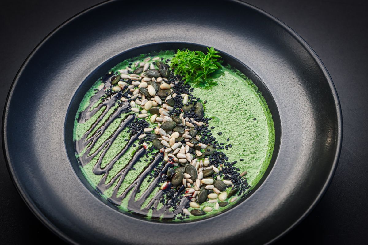 Green soup in a dark bowl with a seed garnish